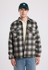 Geruite flanellen shirt in groene, bruine en witte tinten, met een knoopsluiting aan de voorkant, twee borstzakken en een relaxte pasvorm. Draag het over een beige trui.