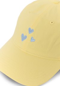 Casquette de baseball jaune avec trois petits cœurs bleus brodés sur la face avant, au-dessus de la visière.