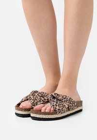 Sandales à imprimé léopard avec un dessus en tissu tordu, semelle en jute tissée plate et semelle extérieure en caoutchouc noir contrastant. Design décontracté et à bout ouvert.