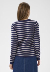 Langärmliges Shirt mit marineblauen und beigen Streifen, mit rundem Ausschnitt und figurbetontem Schnitt, kombiniert mit einem Jeansrock.