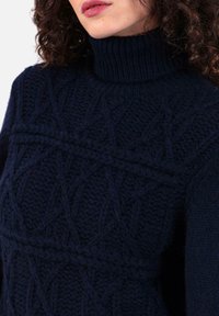 Pull en laine tricotée bleu marine foncé avec un col montant côtelé, des motifs texturés et une coupe décontractée. Laine douce et épaisse avec des mailles en relief.