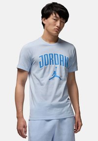 T-shirt di cotone azzurro chiaro con audace testo "JORDAN" in blu scuro e un logo silhouette. Collo rotondo e maniche corte. Vestibilità casual.