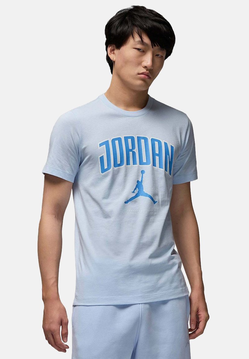 T-shirt di cotone azzurro chiaro con audace testo "JORDAN" in blu scuro e un logo silhouette. Collo rotondo e maniche corte. Vestibilità casual.