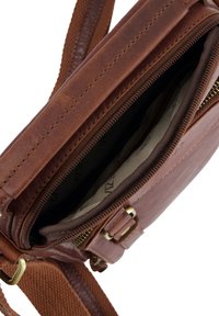 Brązowa skórzana torba na ramię z otwartym zamkiem, ukazującym wewnętrzną podszewkę z tkaniny oraz regulowanym plecionym paskiem z mosiężną klamrą.