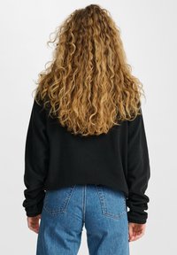Sort oversized sweatshirt med lange ærmer, ribbede manchetter og en cropped søm, parret med højtaljede blå denim jeans.
