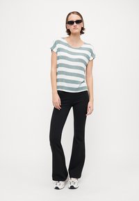 Stripet bomullstop med kort erm i lys grønn og hvit, kombinert med svarte utsvingte bukser og hvite sneakers. Modellen har på seg mørke solbriller.