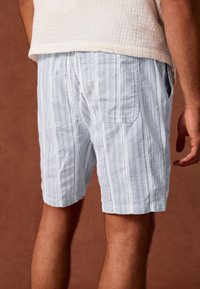 Lichtblauwe korte broek met strepen, gemaakt van gestructureerde stof, met zijzakken en een losse pasvorm, eindigend net boven de knie.