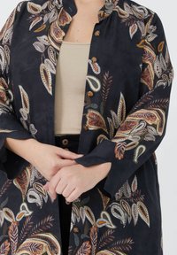 Black patterned jacket featuring colorful leaf designs, round collar, and button closures. Lightweight fabric with a flowing silhouette.