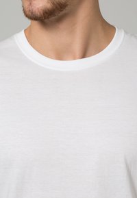 Camiseta blanca de algodón con escote redondo y mangas cortas. La tela parece suave y ligera, con una textura lisa y un diseño minimalista.