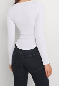 Top bianco a maniche lunghe con design aderente e scollatura rotonda, abbinato a jeans in denim scuro con tasche posteriori e vita alta.