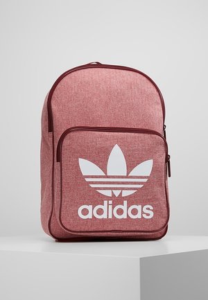 Sac à dos rose Adidas avec une grande poche avant arborant le logo tréfle Adidas blanc et le texte, présenté sur une surface blanche.