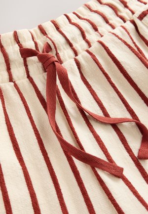 Kreemikas triibuliste kangastega lühikesed püksid, punaste vertikaalsete triipudega. Omavad elastset vöökohaga ja lipsuga kokkuseadmist. Pehme tekstuur.