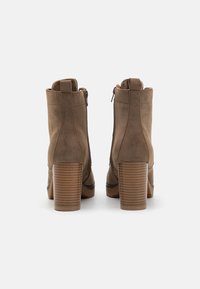 Bottines en daim marron avec un bout rond, des fermetures éclair sur les côtés et des talons en bloc texturés. Le design présente des coutures verticales et une finition lisse.