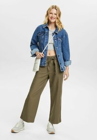 Jeansjakke, grå crop-top, olivengrønne vide bukser og lyse sneakers. Outfittet inkluderer en crossover-veske og har en avslappet passform.