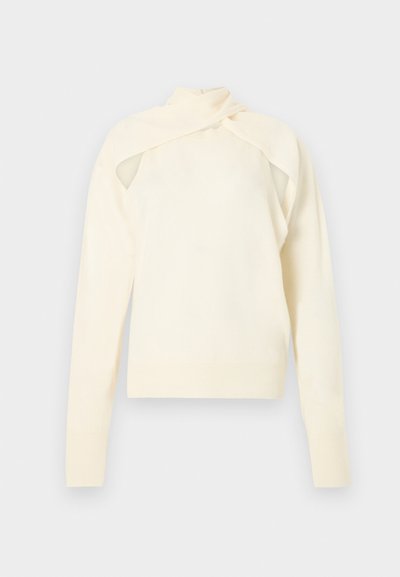 Μακρυμάνικο πλεκτό τοπ σε κρεμ απόχρωση με κομμένο σχέδιο στους ώμους και λεπτομέρεια γιακά που τυλίγεται γύρω, παρουσιάζεται σε ουδέτερο φόντο.