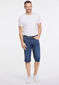 Shorts de mezclilla en azul oscuro con un corte informal, que cuentan con cinco bolsillos, costuras en contraste, y combinados con una camiseta blanca simple y zapatillas blancas.