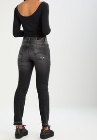 Musta pitkähihainen paita, jossa on matala selkä. Harmaat skinny-farkut, joissa on kulutusedustuksia, istuva malli ja käännetyt lahkeet. Mustat sneakerit, joissa on tekstuuria.