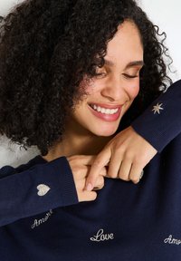 Suéter azul marino hecho de tela suave, con acentos bordados en plata que incluyen corazones y las palabras "Amor" y "Amour."