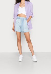 Ljuslila kavaj över en vit kort topp, tillsammans med ljusblå shorts med knytbälte. Bärs med vita platåskor.