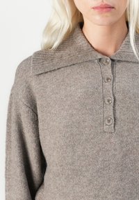 Jasnobrązowy sweter z dzianiny z fakturowanym, oversize'owym kołnierzem i pięcioma guzikami. Miękka tkanina z delikatnym melanżowym wzorem.