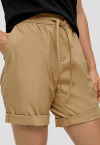Szkatułkowe szorty z elastycznym pasem i sznurkiem do regulacji. Posiadają wykończone mankietem nogawki oraz kieszenie boczne. Gładki, lekki materiał.