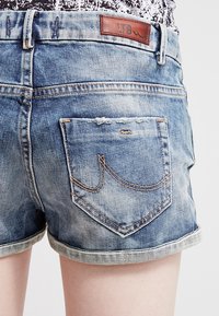 Krótkie spodenki dżinsowe w wyblakłym niebieskim kolorze z podwiniętymi nogawkami, wyposażone w skórzaną naszywkę z logo LTB oraz pojedynczą tylną kieszeń z detalami szwów.