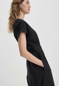 Vestido negro de algodón con mangas cortas, corte relajado y bolsillos laterales. Presenta una cintura ceñida con cinturón y una textura suave.