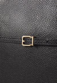 Musta nahkalaukku, jossa on kivenkaltaista pintaa ja kullanvärinen suorakulmainen solki. Suunnittelu on tyylikäs ja minimalistinen.