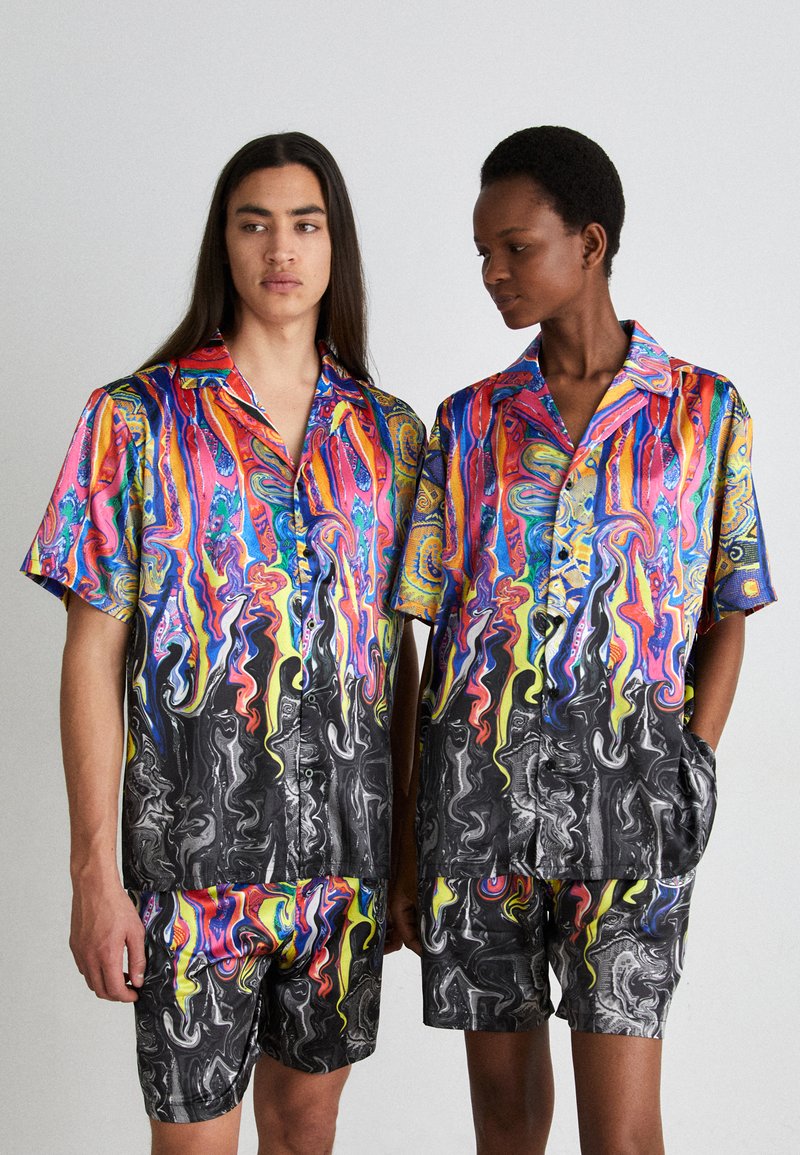 Magliette a maniche corte multicolore con motivi e pantaloni corti in colori vivaci, caratterizzati da spirali astratte e una base nera con texture lucida.