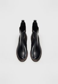 Bottines noires en cuir avec un design épuré, des panneaux latéraux texturés et des coutures brunes le long des semelles.