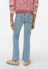 Svijetloplave trapezaste traperice s visokim strukom, pet džepova i izblijedjelim završetkom. Nošene s bež cipelama i ružičastim puloverom s uzorkom.