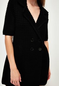 Černé blazer šaty s texturou, V-výstřihem, krátkými rukávy, dvouřadým zapínáním a kulatými černými knoflíky. Měkká, tkaná látka.