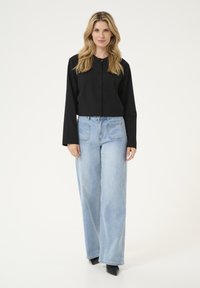 Schwarze kurze Jacke mit Knopfverschluss, kombiniert mit hellblauen weiten Jeans mit Fronttaschen und klassischer Denim-Struktur.