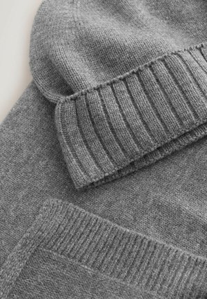 Căciulă tricotată gri cu tiv ribbit și o textură moale, stratificată peste un pulover gri cu un design neted, uniform.