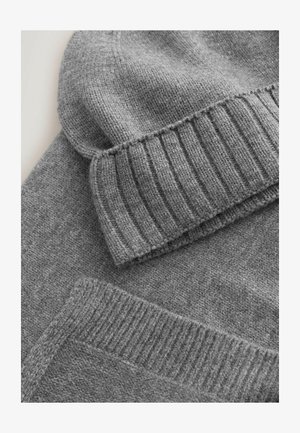 Sivá pletená čiapka s rebrovaným lemom a jemnou textúrou, položená na sivej mikine s hladkým, jednofarebným dizajnom.