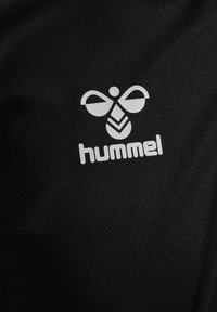 Svart atletisk tyg med en framträdande vit logotyp av en bi med stiliserade vingar och varumärket "hummel" nedanför.