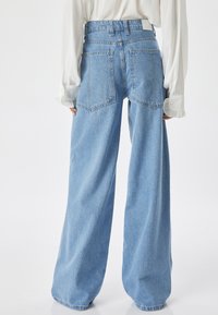 Jeans de denim de pierna ancha en azul claro. Presentan una cintura alta, dos bolsillos traseros y una textura ligeramente desgastada. Diseño clásico de cinco bolsillos.