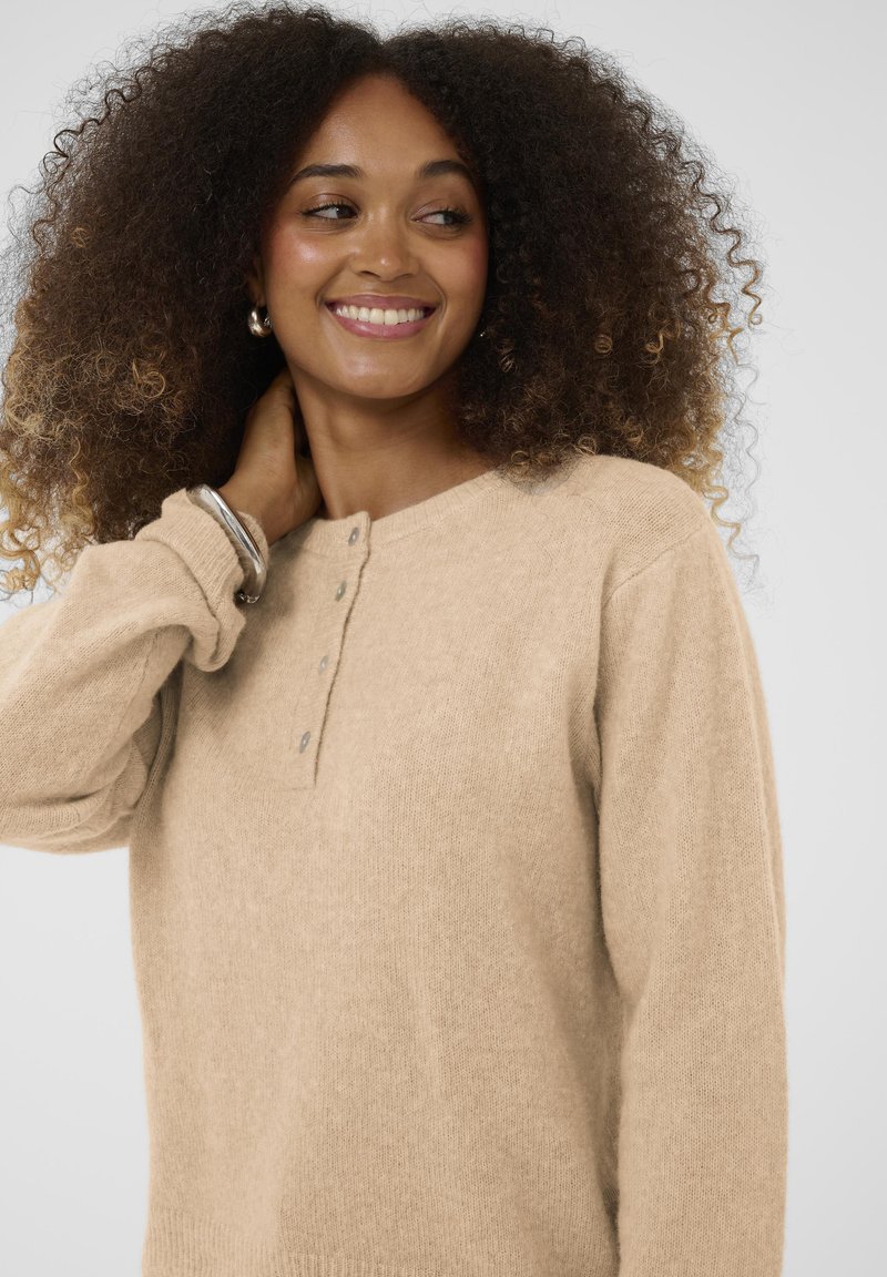 Maglione beige a maglia con scollo rotondo, maniche lunghe e chiusura a tre bottoni. Tessuto morbido e vestibilità rilassata.