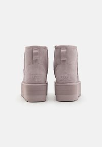 Bottes en daim lilas avec une tige courte, dotées d'une semelle plateforme et d'une languette à l'arrière ; logo UGG embossé sur le talon.