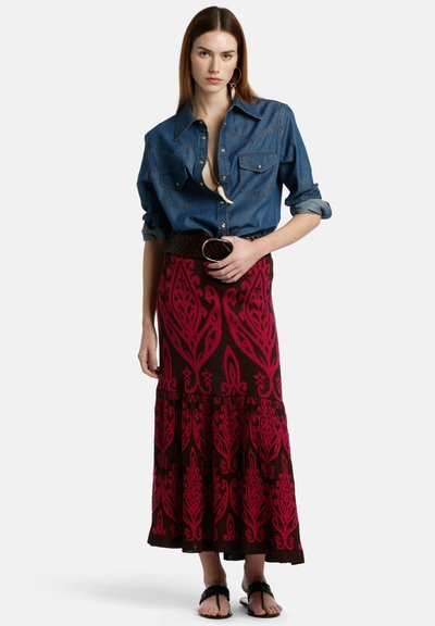 Denim srajca z gumbi v kombinaciji z dolgo rjavo krilo z drznimi roza cvetličnimi vzorci. Model nosi sandale in drži okroglo zaponko za pas.