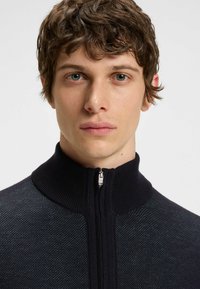 Navy Zip-Up-Pullover mit hohem Kragen und strukturiertem Strickmuster, an der Vorderseite mit einem glatten Reißverschluss und einer taillierten Passform.