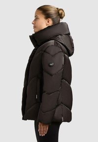 Giacca invernale nera imbottita con colletto alto, motivo a chevron, tasche laterali e patch con logo sulla manica. Tessuto morbido e lucido.
