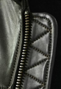 Schwarzes Lederetui mit Reißverschluss, das mit gesteppten, dreieckigen Mustern und kontrastierenden Nähten versehen ist. Es hat einen metallischen Reißverschluss und eine glatte Oberfläche.