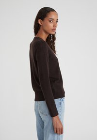 Dunkelbrauner Pullover mit langen Ärmeln, Rundhalsausschnitt und geripptem Saum, kombiniert mit hellblauen Jeans. Glatte Textur, lässige Passform.