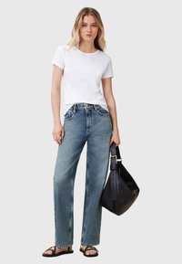 T-shirt bianco a maniche corte abbinato a jeans a gamba larga di colore blu chiaro, con una borsa a spalla in pelle nera e sandali neri.