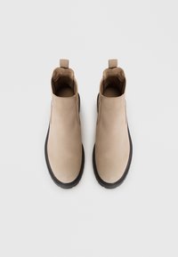 Stivali alla caviglia beige con un upper in pelle liscia, pannelli laterali elasticizzati e una suola in gomma nera testurizzata. Maniglia circolare sul retro.