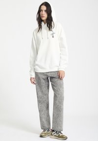 Haut à capuche blanc avec une poche avant et un cordon de serrage ajustable. Associe à un pantalon en denim gris clair avec une texture délavée et des jambes larges.