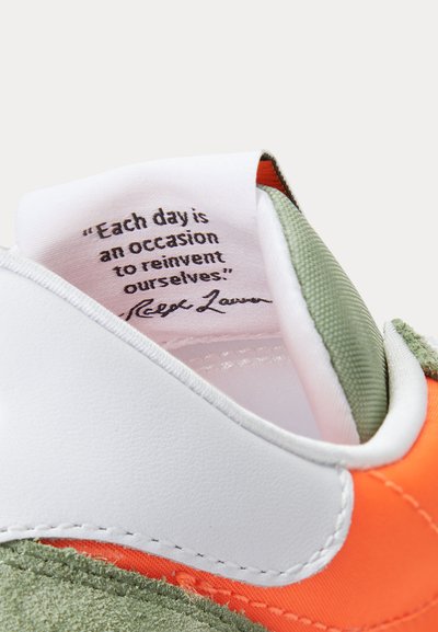 Tuva balta, oranža un zaļa sneaker mēle ar Ralph Lauren citātu: "Katru dienu ir iespēja sevi pārradīt."