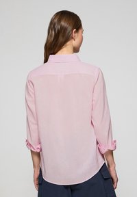 Camicia rosa chiaro con colletto, maniche arrotolate e design a schiena dritta. Realizzata in un tessuto leggero con una consistenza morbida.