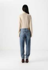 Beige, knit turtleneck sweater with a relaxed fit. Light blue, high-waisted, loose-fit jeans. Brown block-heeled shoes.